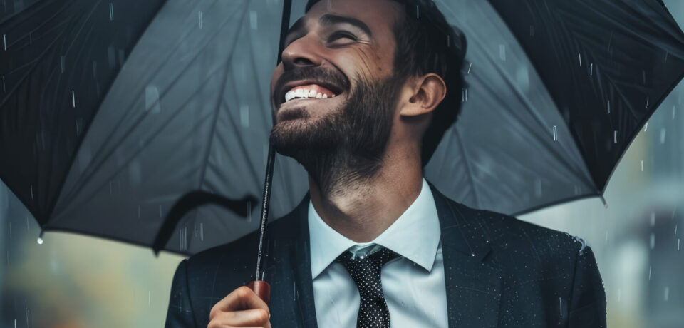 Closeup happy smiling businessman holding umbrella on the street, rain. Creative concept of business insurance against losses